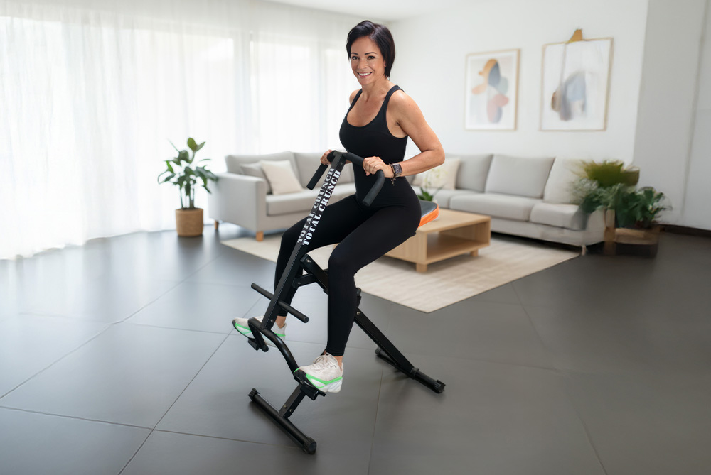 Frau trainiert zu Hause auf dem Total Crunch Ganzkörper-Trainingsgerät in modernem hellen Wohnzimmer